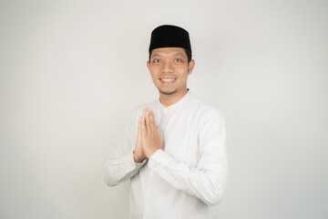 Happy smiling Asian Muslim man in Arabic costume standing with Eid greeting gesture and welcoming Ramadan isolated background - obrazy, fototapety, plakaty