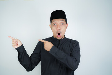 Wow face shocked expression Asian Muslim man pointing hand finger at empty space on isolated background - obrazy, fototapety, plakaty
