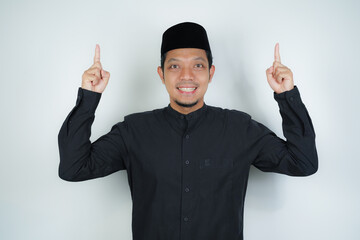 Cheerful handsome Asian Muslim man pointing hand finger at empty space for advertising on isolated background - obrazy, fototapety, plakaty