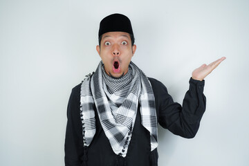 Wow face shocked expression Asian Muslim man wearing Arab turban sorban pointing hand finger at empty space on isolated background - obrazy, fototapety, plakaty