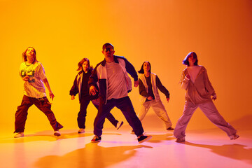 Group of dancers in streetwear performing hip-hop moves in neon light against gradient colorful...