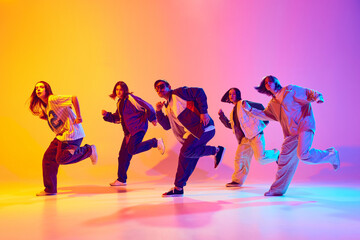 Urban dance crew in casual outfits in mid-dance in neon light against gradient colorful studio...