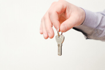 Hand holding house keys. Moving house, relocation. Caucasian male hand holding key to house on white background. Copy space