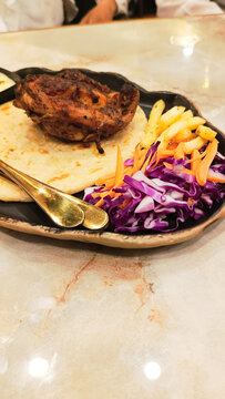 dajaj mashwi, oven roasted chicken typical arab dish served with 2 khubus (pita bread), french fries, closeup of salad, chili sauce and thum with empty space above the bottom