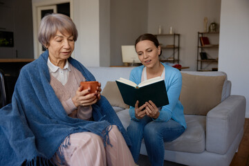 Smiling adult daughter reading for old mother with mental disorder