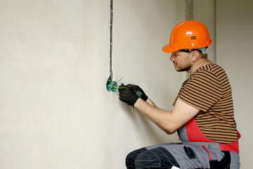 Electrician male in uniform, protective gloves and helmet checks presence of electrical voltage in...