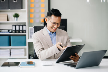 Asian man using laptop and tablet while sitting at her working place. Concentrated at work.
