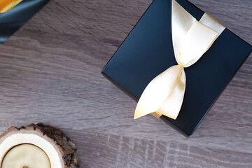 wooden candle and black present box with yellow bow on brown background