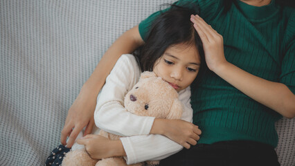 A young girl is laying on a couch with a teddy bear in her arms