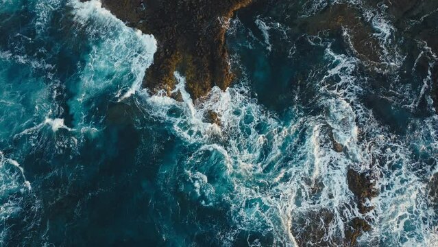 waves splashing against the cliffs at sunset top shot aerial view