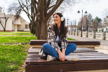 One young girl or woman is listening to music on her wireless headphones and enjoying the sun outdoors	
