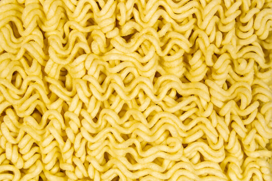 A close up of yellow ramen noodles. The noodles are long and thin, and they are arranged in a way that makes them look like they are curled up. The image has a warm and inviting mood