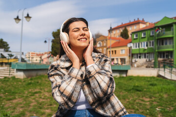 One young girl or woman is listening to music on her wireless headphones and enjoying the sun outdoors	
 - obrazy, fototapety, plakaty