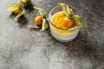 Creamy panna cotta and fresh goldenberry garnishing, cold dairy dessert in glass with fruity puree