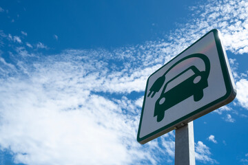 Low angle view of an electric car recharging point road sign, against a blue sky with white clouds.