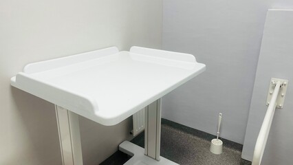 metal handrails and changing table in a toilet in a hospital with gray walls. side view