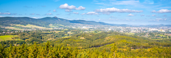 A sweeping vista of Liberec city nestled between rolling hills and Jested ridge under a blue sky dotted with clouds. - 769601888