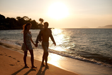 Love, sunset sky and couple walking at ocean for tropical holiday adventure, relax and bonding together. Nature, man and woman on romantic date with beach, island and evening waves on happy vacation.