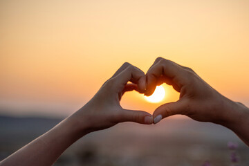 woman creates form a heart shape with hands at sunset. Conveying serene sunset ambiance with heart gesture.