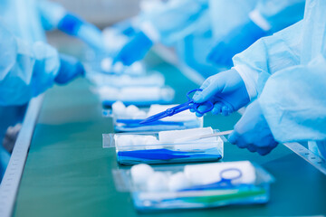 Surgery kit on conveyor line, closeup of medical staff gloved hands sorting blue med instrument...