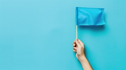 A hand is holding a small blue flag against plain background.