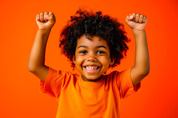 Happy young African American boy with curly hair raising his arms in a victorious gesture on orange background - obrazy, fototapety, plakaty