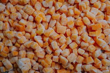 Dense arrangement of frozen pumpkin cubes covered with frost, displaying a bright orange hue.
