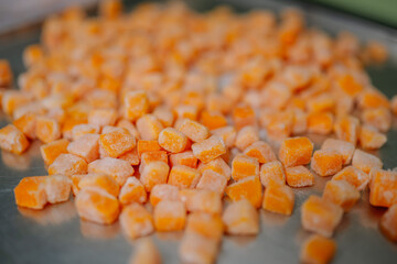 Scattered cubes of frozen pumpkin on a tray, dusted with frost, showcasing a vibrant orange color.