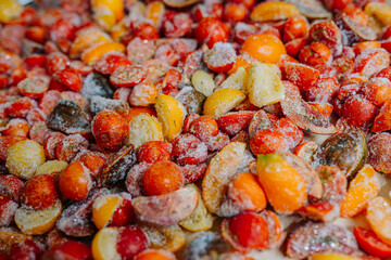 Heap of halved, frosty tomatoes with ice crystals, in a mix of red and yellow colors.