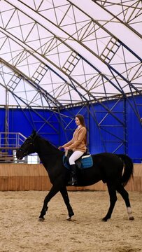 Long-haired woman riding a beautiful black horse. Female lady coach walks in front of animal. Young girl comes up to the foreground. Vertical video