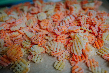 Close-up of a pile of various colored freeze-dried waffle-cut vegetables on a baking sheet.
