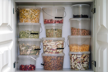 A pantry shelf stocked with clear containers filled with various dehydrated fruits and vegetables.