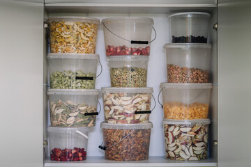 A pantry shelf stocked with clear containers filled with various dehydrated fruits and vegetables.