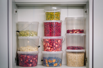 a pantry shelf stocked with clear, stackable containers filled with various dried fruits and grains.