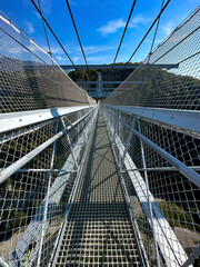 Obraz premium Clear sky over a pedestrian suspension bridge with protective nets, leading into lush greenery.