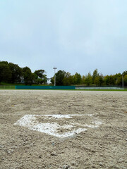 Close-up of a sand covered home plate with a view of the baseball field from behind the plate,...