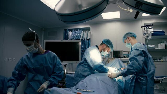 A surgeon and surgical team perform cosmetic breast surgery in a modern hospital operating room. Breast augmentation. Cosmetic surgery. Urgent Care.