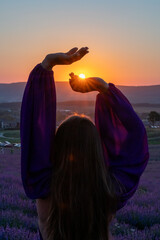 Woman raises arms in lavander field at sunset enjoys sunset in purple flower field. Serene floral setting. Setting sun. Conveying peaceful ambiance in flower field at sunset.