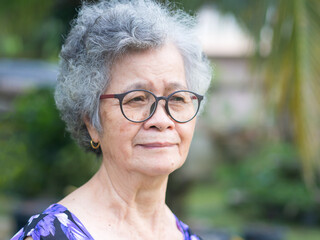 Beautiful elderly Asian woman looking away with a smile while standing in the garden.