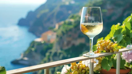 Foto op Canvas A glass of white wine on a balcony with scenic view coastal cliff and the sea. © Artyom