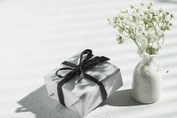 White gift box and vase with gypsophila on the table in the sun. Happy holidays concept.