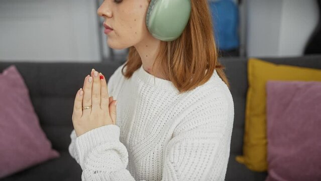 Young woman in sweater enjoys music on headphones with eyes closed indoors