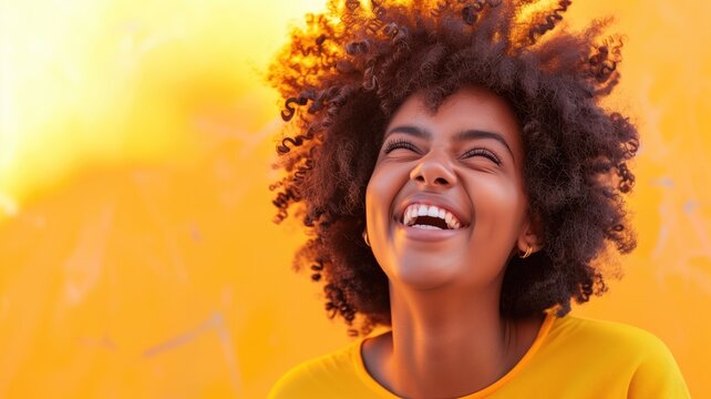 Joyful woman with curly hair laughing against a warm orange background.