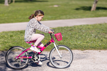 A young girl is riding a pink bike with a basket on the front - obrazy, fototapety, plakaty