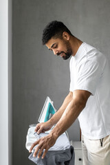 Handsome black man ironing and looking into his clothes in his bedroom