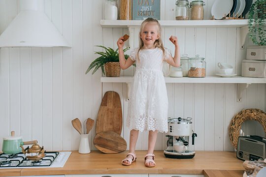 Joyful girl standing on a kitchen counter, in a white lace dress, surrounded by rustic kitchen decor