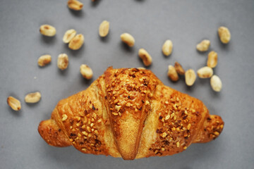 Croissant with peanut crumbs and cream next to scattered peanuts