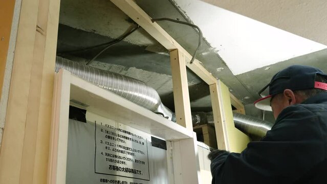 内装工事　天井裏のダクトホースを取り付ける作業員