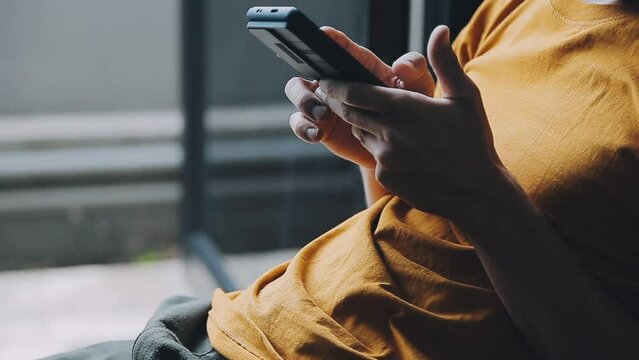Silhouette of cropped shot of a young man working from home using smart phone and notebook computer, man's hands using smart phone in interior, man at his workplace using technology, flare light