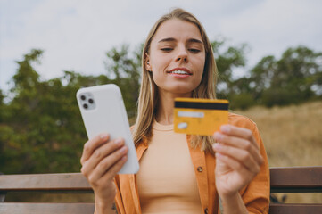 Young minded woman wears orange shirt casual clothes using mobile cell phone hold credit bank card...